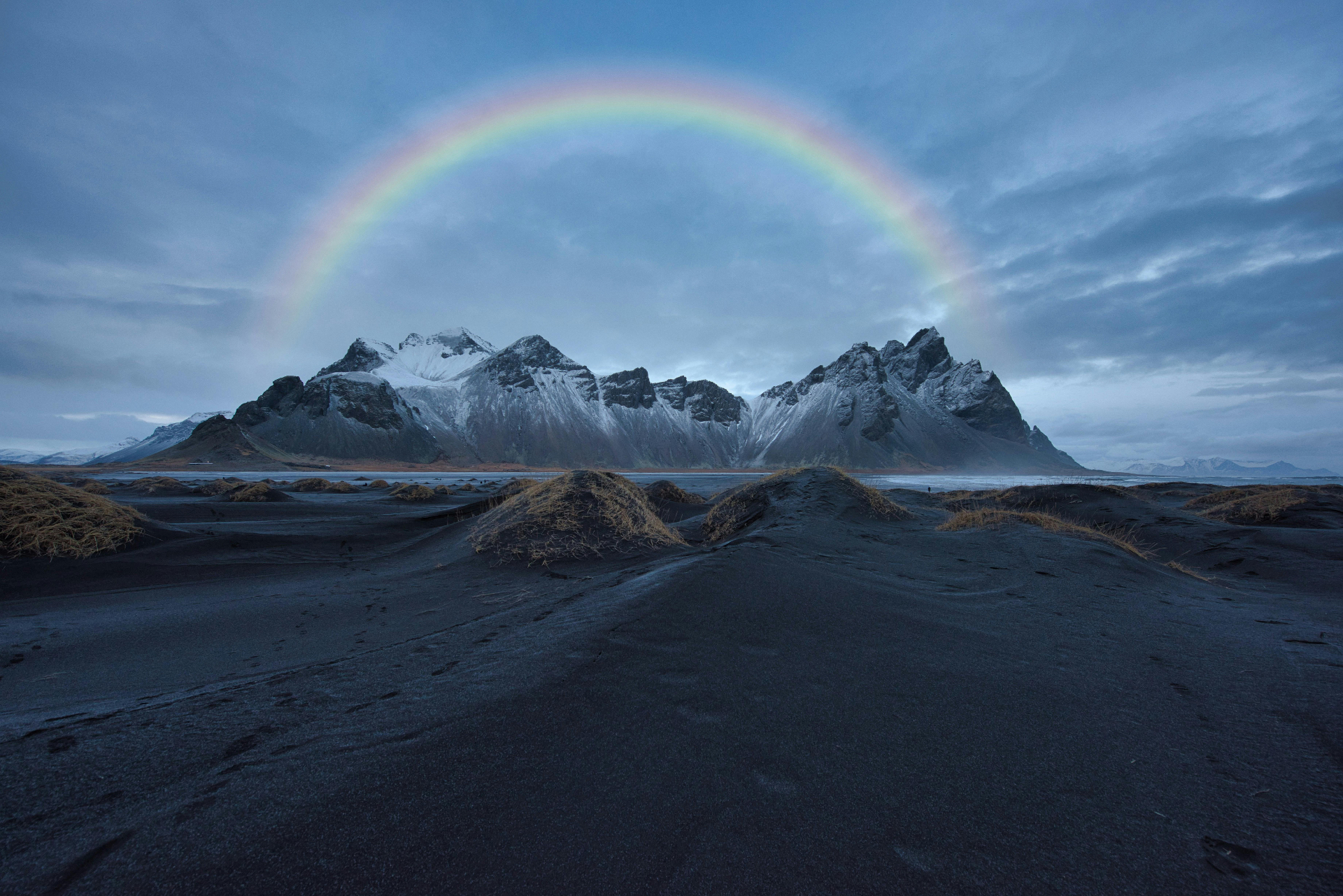 Rainbow over dramatic mountains and dark volcanic sand